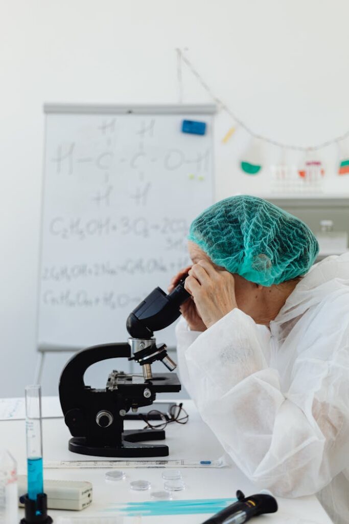 Researcher in protective gear using a microscope in a laboratory setting for chemical analysis.